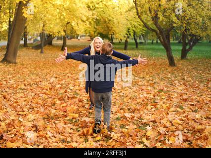 Mère et fils jouent ensemble dans le parc d'automne. Le garçon court vers sa mère, sa mère doit l'attraper Banque D'Images