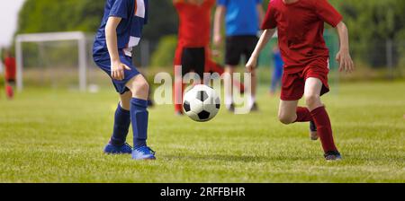 Jeunes joueurs de football Kicking Ball sur le terrain de soccer. Arrière-plan horizontal de soccer. Les jeunes athlètes junior en rouge et bleu Juniors Banque D'Images