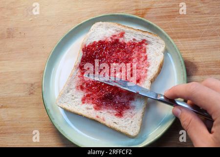 Une photo de quelqu'un étalant de la confiture sur un morceau de pain blanc. Banque D'Images