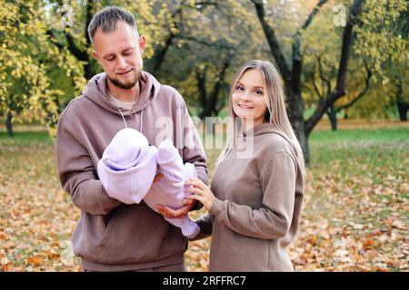 La jeune mère et le père marchent avec un nouveau-né dans le parc d'automne. Père regarde tendrement l'enfant, mère regarde dans la caméra Banque D'Images