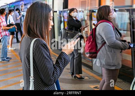 Passager avec téléphone portable à la gare Skytrain, Chong Nonsi, Bangkok, Thaïlande Banque D'Images