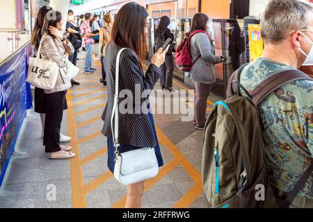 Passager avec téléphone portable à la gare Skytrain, Chong Nonsi, Bangkok, Thaïlande Banque D'Images