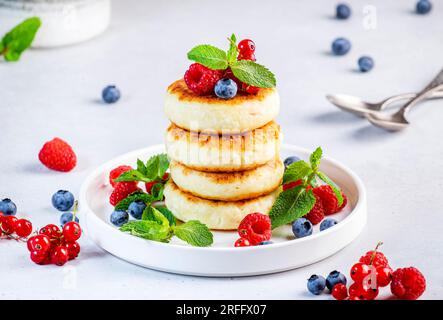 Crêpes épaisses au fromage cottage avec des myrtilles, des framboises et des groseilles rouges, décorées avec de la menthe sur une assiette blanche, délicieux petit déjeuner. Table grise Banque D'Images