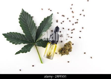 Une feuille fraîche verte de marijuana médicale, à côté se trouve une bouteille en verre d'extrait d'huile de cbd avec une pipette et un bourgeon sec. Graines sur fond blanc. Banque D'Images