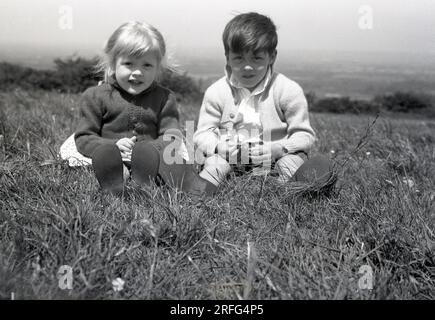 Années 1950, historique, été et deux jeunes enfants, frère et sœur, assis ensemble sur une colline herbeuse, Angleterre, Royaume-Uni. Banque D'Images