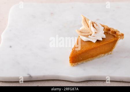 Tranche d'une tarte à la citrouille traditionnelle pour Thanksgiving garnie de crème fouettée sur fond clair Banque D'Images