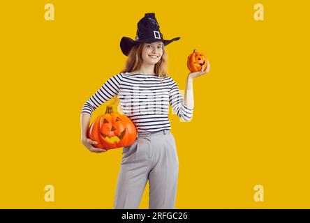 Jeune femme attirante d'âge étudiant tient deux potirons d'Halloween stands sur fond de studio orange Banque D'Images