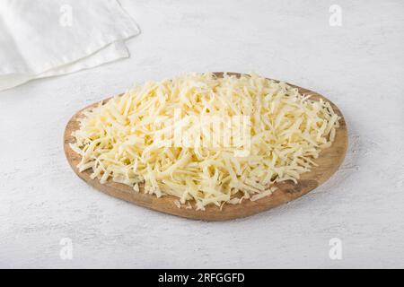Planche de bois avec fromage à pâte dure râpé sur un fond gris clair. Cuisiner de délicieux plats végétariens. Banque D'Images