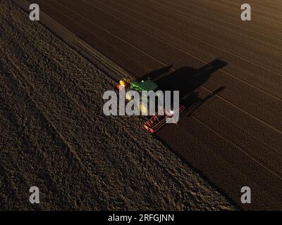 Un tracteur John Deere ensemence un champ précédemment cultivé avec du maïs doux, tard dans la soirée. Banque D'Images