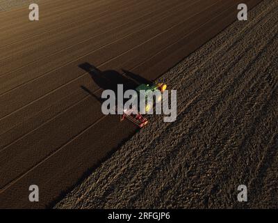 Un tracteur John Deere ensemence un champ précédemment cultivé avec du maïs doux, tard dans la soirée. Banque D'Images