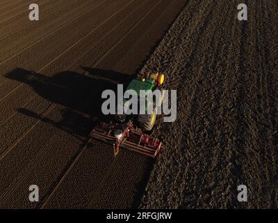 Un tracteur John Deere ensemence un champ précédemment cultivé avec du maïs doux, tard dans la soirée. Banque D'Images