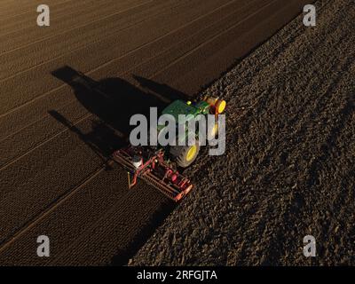 Un tracteur John Deere ensemence un champ précédemment cultivé avec du maïs doux, tard dans la soirée. Banque D'Images