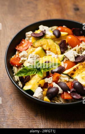 Plat fait maison avec des légumes d'été grillés avec des olives noires et feta végétalienne sur pesto orzo. Banque D'Images