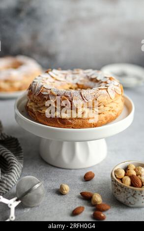 Dessert français classique de forme ronde Paris Brest aux amandes et noisettes sur une assiette blanche. Banque D'Images