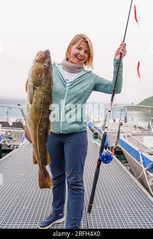 Heureuse pêcheuse tenant une grosse morue arctique. Norvège pêche heureuse. Femme avec du poisson de morue dans les mains Banque D'Images