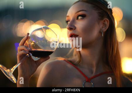 Portrait en gros plan d'une jeune femme dans la vingtaine portant une robe orange, tenant un verre rempli de vin rouge Banque D'Images