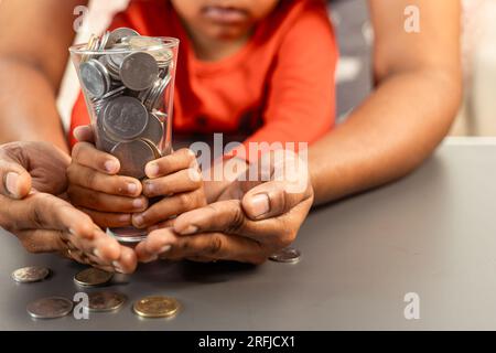 Une jeune femme indienne et sa fille tiennent un verre rempli de pièces de roupie indienne Banque D'Images