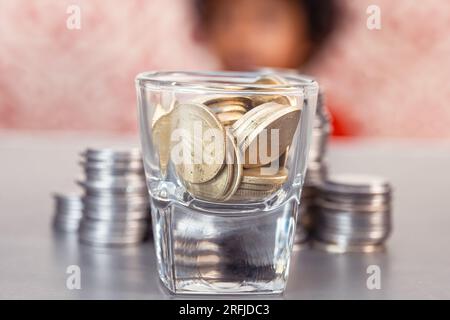 Cette image stock montre une pile de pièces de monnaie avec des enfants assis en arrière-plan, floue Banque D'Images