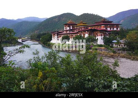 Punakha Dzong historique du Bhoutan vu de l'autre côté de la rivière Mo Chhu avec le pont cantilever en bois restauré visible sur la gauche et les montagnes au-delà Banque D'Images