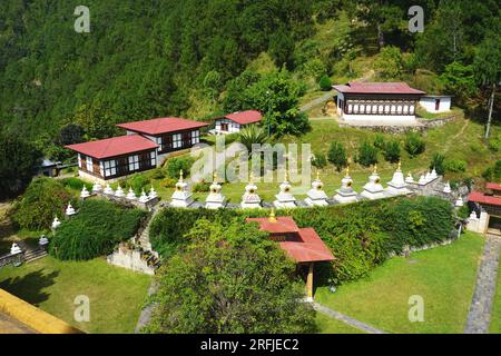 Une rangée de stupas commémoratifs blancs assortis entourent plusieurs bâtiments sur une colline en terrasses à Khamsum Yulley Namgyal Chorten, Royaume du Bhoutan Banque D'Images