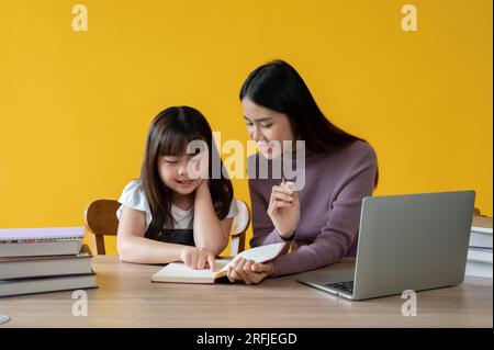 Une adorable jeune fille asiatique aime apprendre l'anglais avec une enseignante, assise à une table ensemble. fond jaune isolé. Banque D'Images