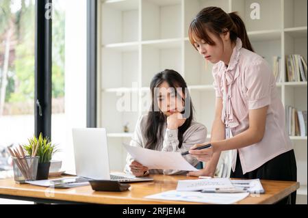 Deux femmes d'affaires asiatiques concentrées ou comptables discutent du travail, analysent les données de vente et travaillent ensemble au bureau. Banque D'Images