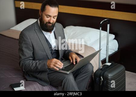 L'homme voyageur s'assit avec un ordinateur portable sur le lit Banque D'Images