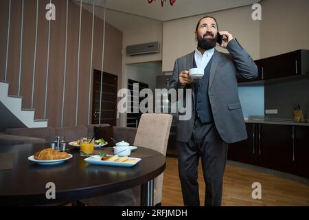 L'homme se tient à une table avec un téléphone et du café Banque D'Images