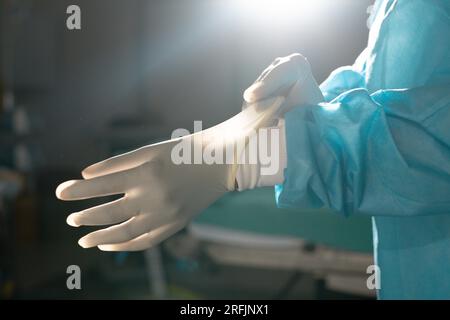 Section médiane d'une chirurgienne biraciale portant une blouse et des gants en salle d'opération Banque D'Images