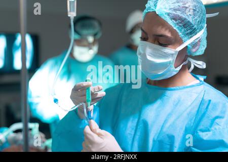 Chirurgien biracial portant une blouse de chirurgie appliquant le goutte-à-goutte en salle d'opération à l'hôpital Banque D'Images