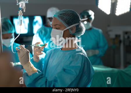 Chirurgien biracial portant une blouse de chirurgie appliquant le goutte-à-goutte en salle d'opération à l'hôpital Banque D'Images