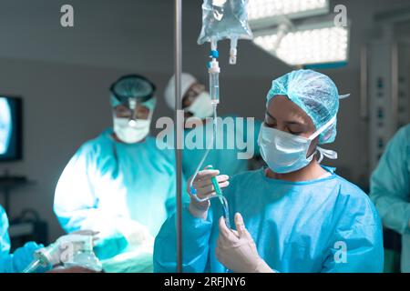 Chirurgien biracial portant une blouse de chirurgie appliquant le goutte-à-goutte en salle d'opération à l'hôpital Banque D'Images