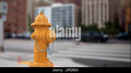 Bouche d'incendie de couleur jaune dans le centre-ville, closeup. Équipement de lutte contre l'incendie, flou de fond urbain Banque D'Images