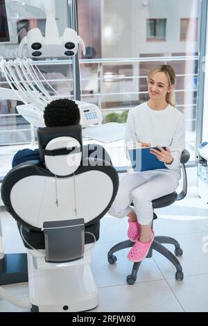 Femme confiante stomatologue gardant des dossiers médicaux écoutant le patient et assis dans un bureau de luxe avec un équipement moderne, un service de clinique privée Banque D'Images