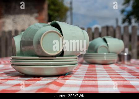 Pile de tasses et soucoupes vert clair sur une table avec une nappe rouge et blanche Banque D'Images