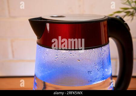 bouilloire électrique moderne avec eau bouillante et condensat sur les murs en verre à la lumière bleue néon Banque D'Images