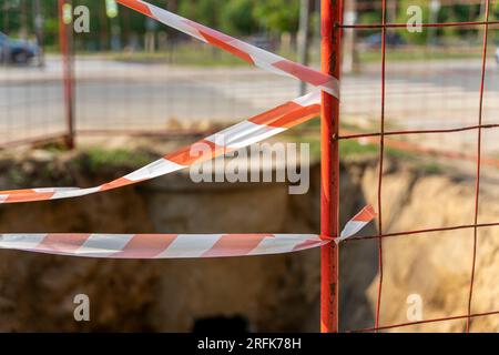 le lieu de réparation sur la rue de la ville est clôturé avec une bande de signalisation rouge et blanche. Travaux de réparation des services publics municipaux. Risque de chute d'une hauteur Banque D'Images