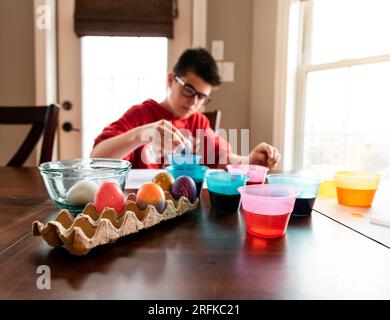 Adolescent mourant oeufs de pâques avec des récipients de colorant à la table. Banque D'Images