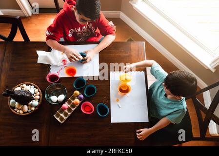 Plan à angle élevé de deux garçons mourant des œufs de pâques colorés à table. Banque D'Images