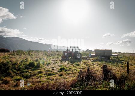 Image d'un tracteur à l'apparence ancienne assis dans un champ avec le soleil derrière. Banque D'Images
