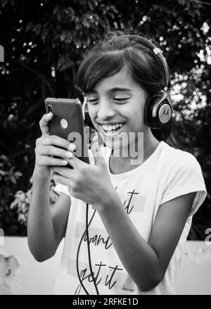 14 octobre 2022 Uttarakhand, Inde. Une jeune fille écoute merveilleusement de la musique sur son smartphone, enfilant un casque. Joie pure dans le rythme. Banque D'Images