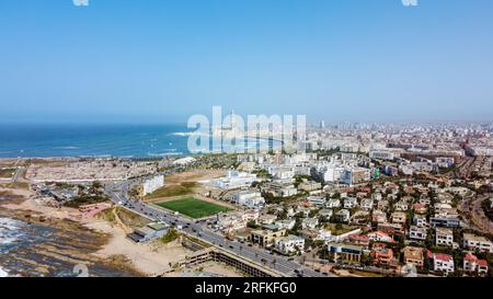 Vue aérienne drone de Casablanca, Maroc. Côte rocheuse de l'océan Atlantique avec bâtiments résidentiels et autoroute, mosquée Hassan II au loin Banque D'Images