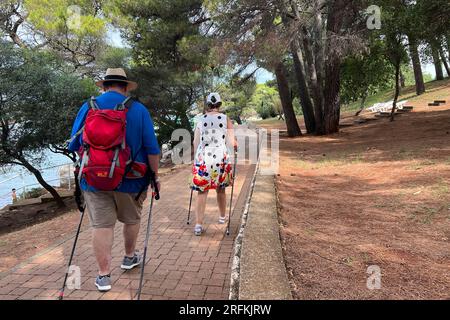 Porec, Kroatien. 01 août 2023. Plava Laguna, côte Adriatique près de Porec/Croatie, plage. Deux personnes, randonneurs, femme et homme Nordic Walking le long de la côte, ? Crédit : dpa/Alamy Live News Banque D'Images