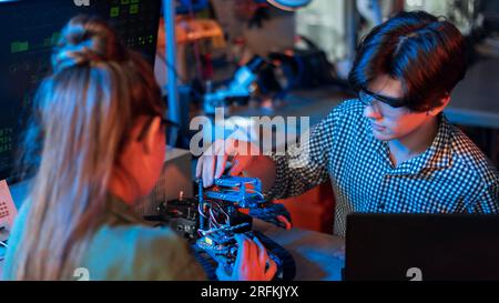 Adolescents faisant des expériences en robotique dans un laboratoire. Garçon et fille dans des lunettes de protection travaillant avec un robot. Éclairage rouge et bleu Banque D'Images