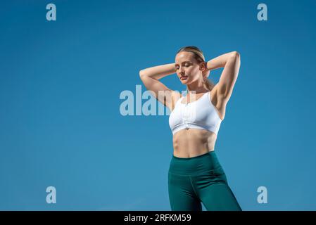 Femme sportive avec ses mains sur la tête, ciel bleu, espace pour le texte. Banque D'Images