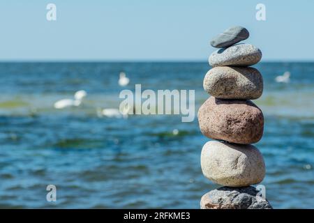 Equilibrer des pierres sur un gros rocher avec de l'herbe de mer sur la plage, avec des vagues d'eau bleue sur fond, mer Baltique, Olando Kepure, Lituanie Banque D'Images