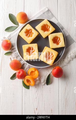 Biscuits mous carrés avec confiture d'abricot gros plan sur une assiette sur la table. Vue verticale de dessus Banque D'Images