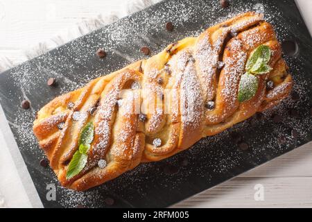 Dessert festif pain sucré tressé avec chocolat et crème anglaise gros plan sur une planche d'ardoise sur la table. Vue de dessus horizontale Banque D'Images