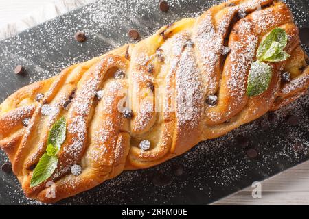 Pain sucré tressé avec chocolat et crème anglaise gros plan sur une planche d'ardoise sur la table. Vue de dessus horizontale Banque D'Images