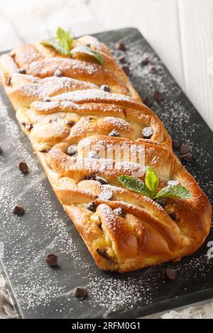 Brioche tressée farcie de chocolat et crème anglaise gros plan sur une planche d'ardoise sur la table. Vertical Banque D'Images